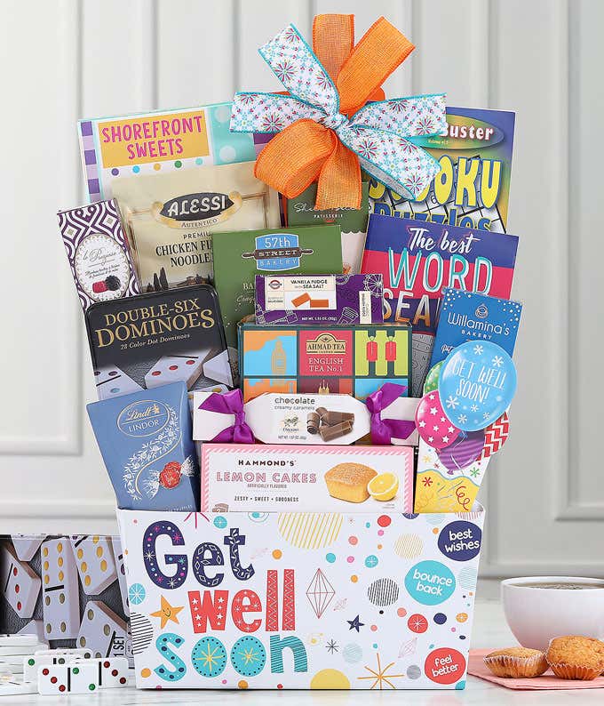 Get well soon gift basket with an orange and blue bow, filled with Ahmad English Tea, baked crackers, soup mix, sweet treats, puzzle books, and a dominoes set, displayed with tea and snacks.