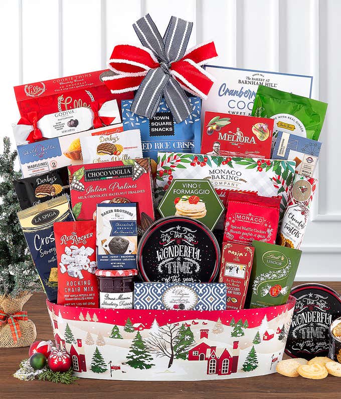 Festive holiday gift basket filled with an assortment of gourmet snacks, cookies, chocolates, and more. Arranged in a red and white Christmas-themed container with village illustrations and topped with a red, white, and navy bow.