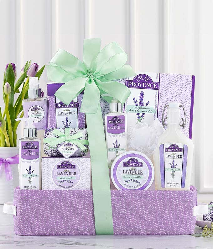 Spa gift basket featuring lavender scented sheet spray, chunky bath salts, bubble bath, body butter, shower gel, and more in a lavender colored gift basket with a green ribbon