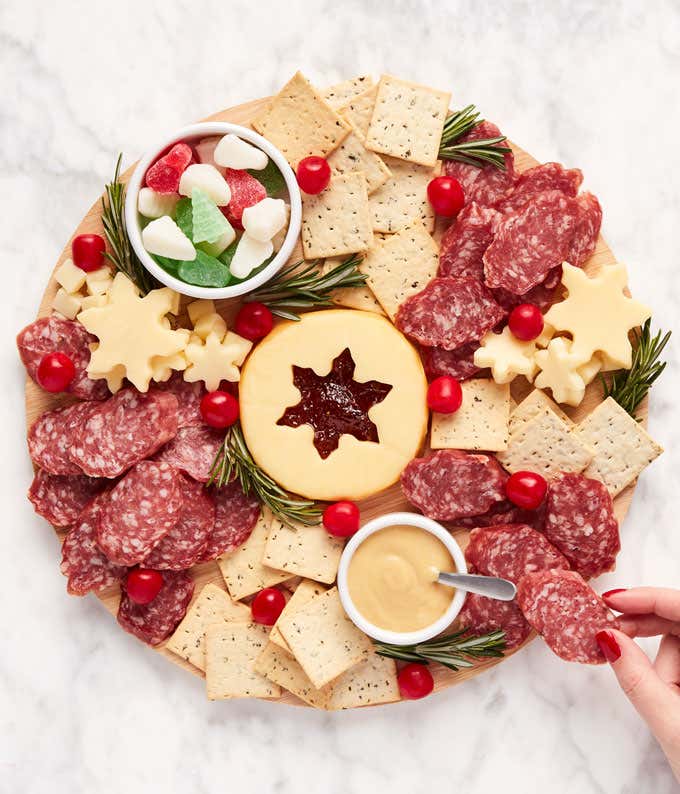 This Holiday Wreath Charcuterie Kit includes crackers, salami, cheese, jam, mustard, candy, a bamboo cutting board, serving bowls, snowflake cutters, and a QR code for video instructions. Ideal for festive gatherings.