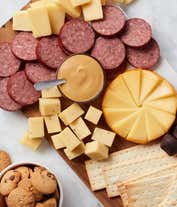 Alternative image 1 for Sympathy gift basket with beef summer sausage, smoked gouda and cheddar cheese, sweet hot mustard, sea salt flatbread, chocolate chip cookies, truffles, and a sympathy ribbon, displayed with a charcuterie-style spread of meats, cheeses, and treats.