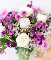 Alternative image 1 for A sophisticated floral arrangement featuring crème roses, lavender alstroemeria, purple stock, purple button chrysanthemums, lavender cushion spray chrysanthemums, white limonium, bupleurum, and huckleberry, all elegantly arranged in a cylinder vase.