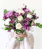 Alternative image 2 for A sophisticated floral arrangement featuring crème roses, lavender alstroemeria, purple stock, purple button chrysanthemums, lavender cushion spray chrysanthemums, white limonium, bupleurum, and huckleberry, all elegantly arranged in a cylinder vase.