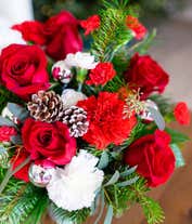 Alternative image 3 for A festive arrangement with red roses (deluxe & premium only), red carnations, white carnations, red mini-carnations, white mini-carnations, seasonal greens, silver ornaments, and pine cones.