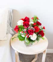 Alternative image 4 for A festive arrangement with red roses (deluxe & premium only), red carnations, white carnations, red mini-carnations, white mini-carnations, seasonal greens, silver ornaments, and pine cones.