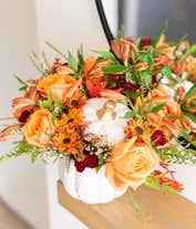 Alternative image 1 for A charming floral arrangement featuring orange roses, orange alstroemeria, maroon mini carnations, yellow mums, and white waxflower, all beautifully arranged in a ceramic pumpkin.