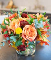 Alternative image 4 for A vibrant fall-themed floral arrangement featuring orange fall roses, orange alstroemeria, yellow button mums, burgundy cushion mums, and orange carnations, all elegantly displayed in a cylinder vase.
