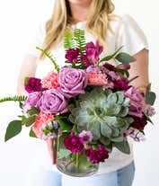 Alternative image 4 for Floral arrangement featuring a succulent plant, pink carnations, purple mini carnations, dark pink roses (in deluxe and premium versions), purple statice, purple alstroemeria, lavender button mums, seasonal greenery, and a personal card message in a glass