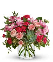 A vibrant floral arrangement featuring pink mini roses, pink alstroemeria, pink mini carnations, a succulent plant, and hot pink roses in deluxe and premium versions. This lush pink mix offers a charming and elegant display.