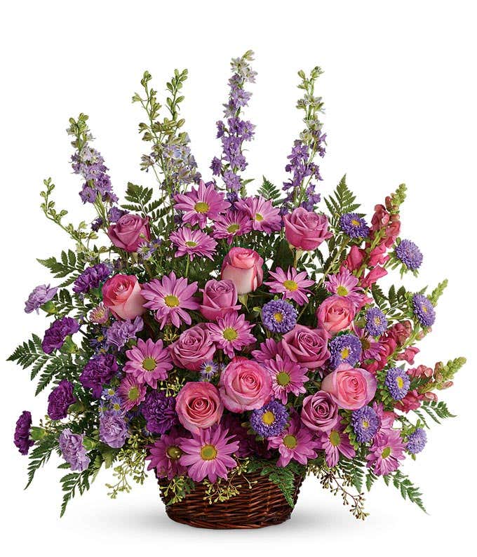 Serene Sympathy floral arrangement featuring Lavender and Pink Roses, Carnations, Larkspur, Snapdragons, Asters, and Daisy Spray Chrysanthemums in a Round Wicker Basket with Handle, offering solace and remembrance during moments of grief.