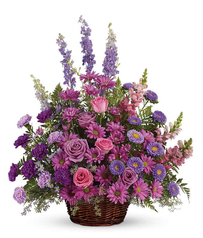 Serene Sympathy floral arrangement featuring Lavender and Pink Roses, Carnations, Larkspur, Snapdragons, Asters, and Daisy Spray Chrysanthemums in a Round Wicker Basket with Handle, offering solace and remembrance during moments of grief.