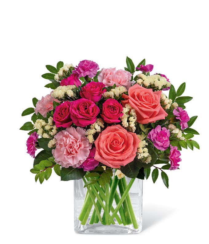 Short, round bouquet of coral, pink, and yellow flowers in a Clear Glass Cube Vase