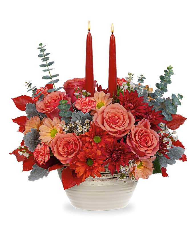 Orange Roses & Carnations, Beige, bronze, and dark bronze chrysanthemums, spiral eucalyptus, red copper beech, and dusty miller in a beige rustic bowl with two burgundy taper candles