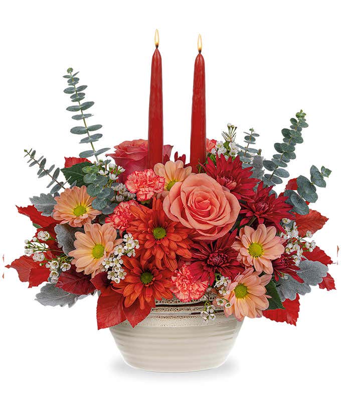 Orange Roses & Carnations, Beige, bronze, and dark bronze chrysanthemums, spiral eucalyptus, red copper beech, and dusty miller in a beige rustic bowl with two burgundy taper candles