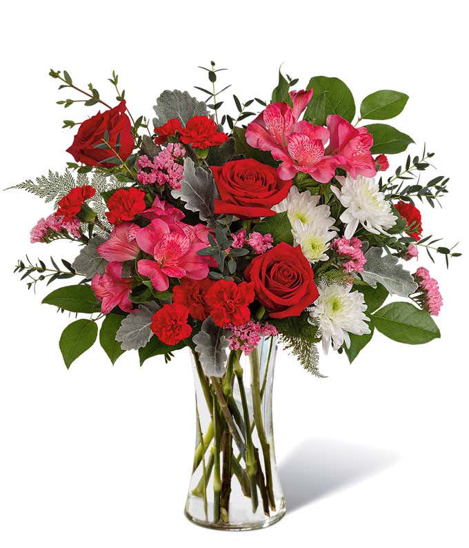 Flowers of red, pink, and white arranged into a tall red sparkly vase.