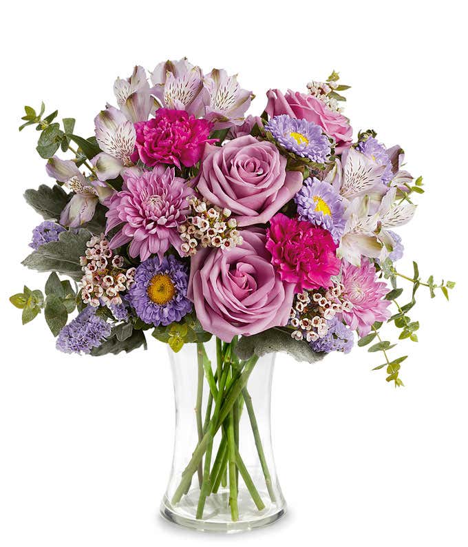 Image of a Mother's Day arrangement featuring Lavender Roses, Lavender Alstroemeria, Fuchsia Carnations, Lavender Matsumoto Asters, Lavender Cushion Spray Chrysanthemums, Lavender Sinuata Statice, Pink Waxflower, floral greens, all beautifully presented i