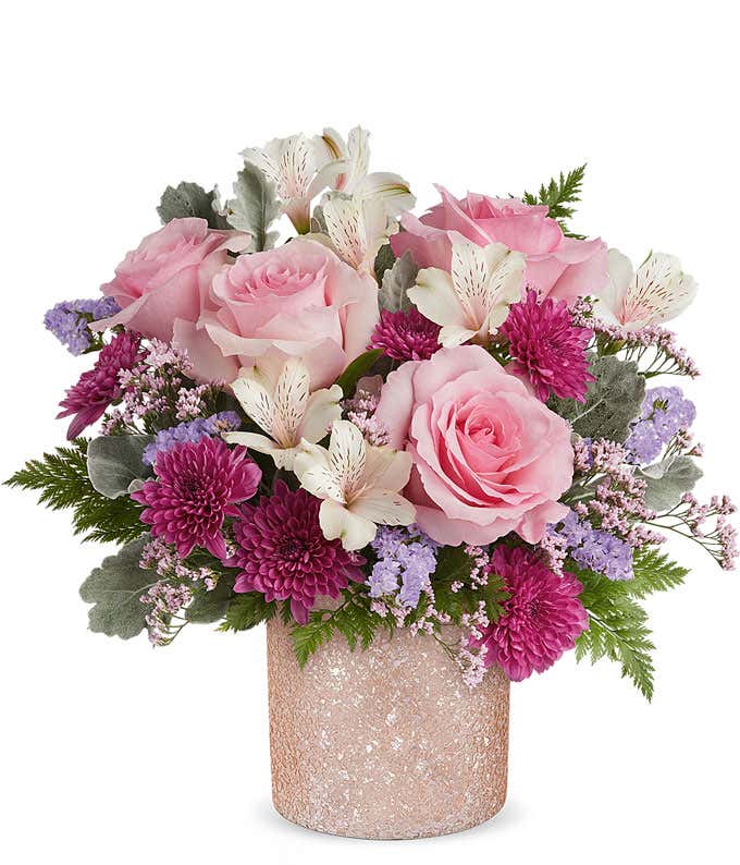 Image of a floral arrangement featuring Pink Roses, Ivory Alstroemeria, Purple Cushion Chrysanthemums, Lavender Sinuata Statice, Pink Limonium, and floral greens, presented in a keepsake Pink Shimmer Vase.