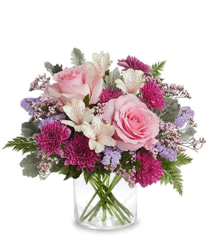 Image of a floral arrangement featuring Pink Roses, Ivory Alstroemeria, Purple Cushion Chrysanthemums, Lavender Sinuata Statice, Pink Limonium, and floral greens, presented in a keepsake Pink Shimmer Vase.
