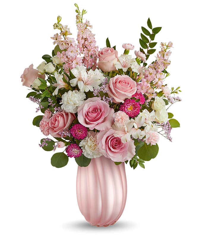 Image of a Mother's Day arrangement featuring Pink Roses, White Spray Roses, White Carnations, Ivory Alstroemeria, Miniature Pink Carnations, Pink Larkspur, Hot Pink Matsumoto Asters, and floral greens, all beautifully presented in a keepsake Pearl Pink S