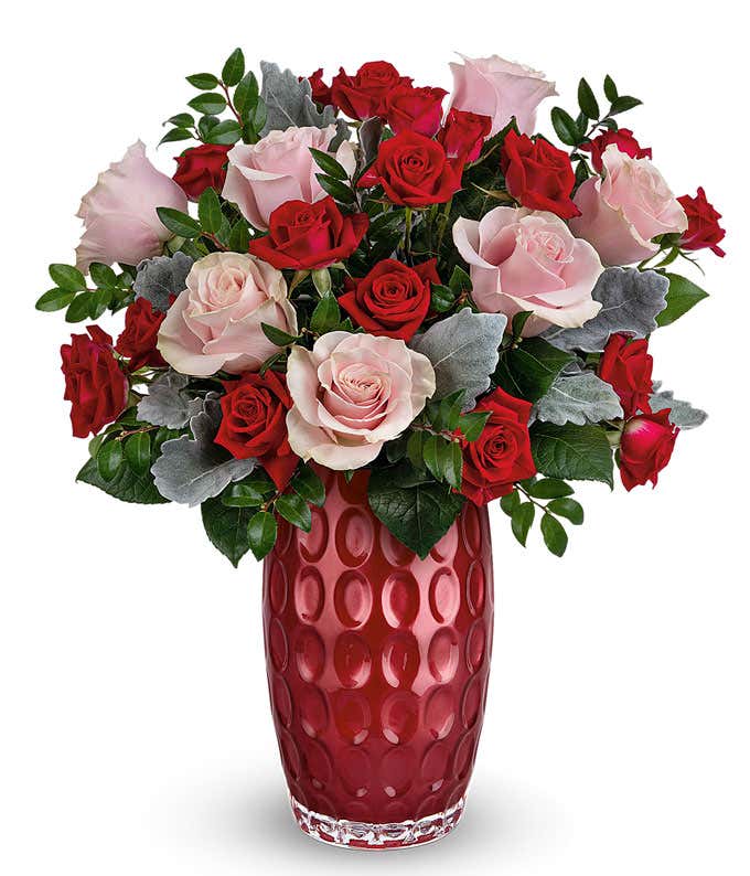 A bouquet with roses with red spray roses with floral greens in a tall red cylinder glass vase