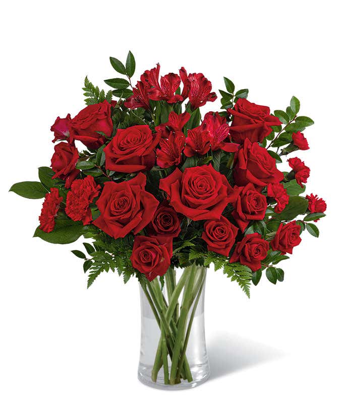 Red roses and red spray roses with floral greens in a tall clear cylinder glass vase