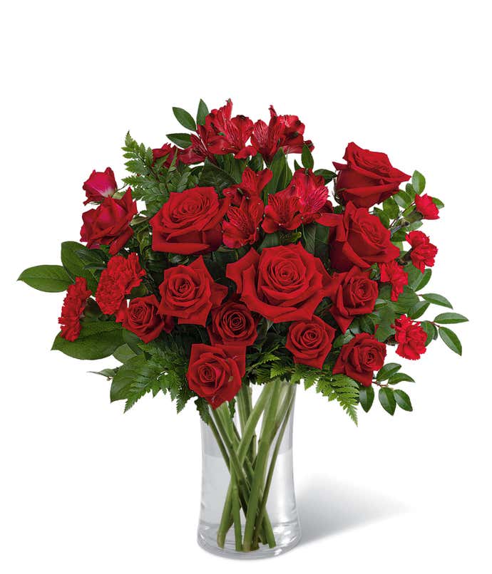 Red roses and red spray roses with floral greens in a tall clear cylinder glass vase