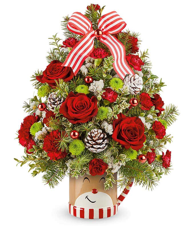 Christmas tree-shaped arrangement with red roses, carnations, pinecones, ornaments, and evergreens in a festive mug topped with a striped bow.