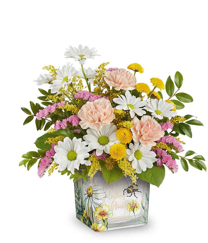 Pink roses, light peach carnations, white daisy spray chrysanthemums, yellow button spray chrysanthemums, pink statice, solidago, and floral greenery arranged in a square glass container featuring a watercolor-style bee and floral design.