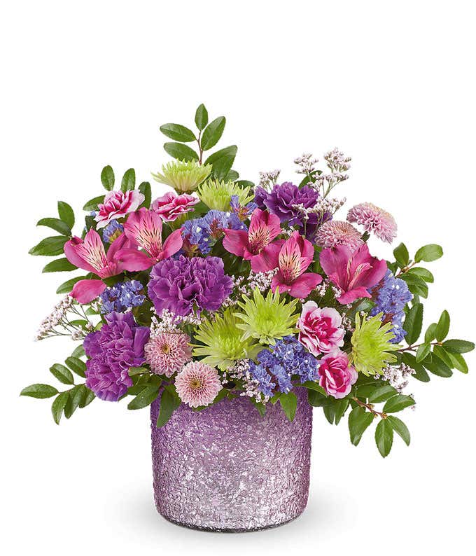 Lavender roses, purple alstroemeria, purple carnations, mini variegated purple carnations, green button spray chrysanthemums, lavender button spray chrysanthemums, purple sinuata statice, and floral greenery arranged in a Glittery Purple vase.