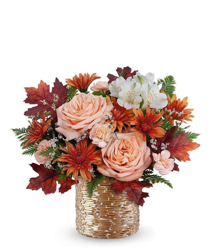 Fall floral arrangement with peach roses, white alstroemeria, bronze cushion spray chrysanthemums, peach miniature carnations, and autumn leaves in a gold-glass textured vase.