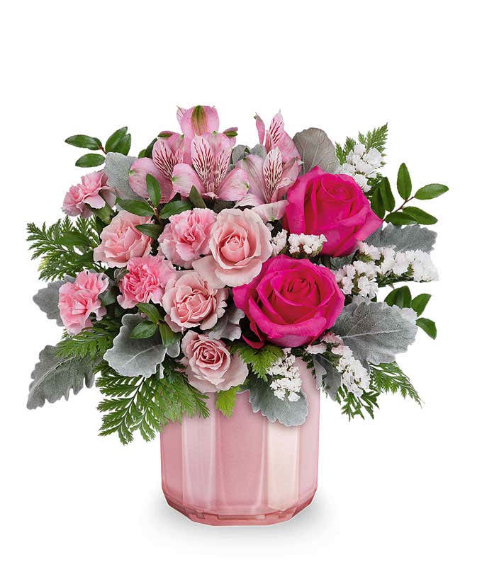 A Valentine's Day bouquet featuring hot pink roses, light pink spray roses, pink alstroemeria, light pink carnations, white filler flowers, dusty miller, and lush greenery, arranged in a soft pink ribbed glass vase.
