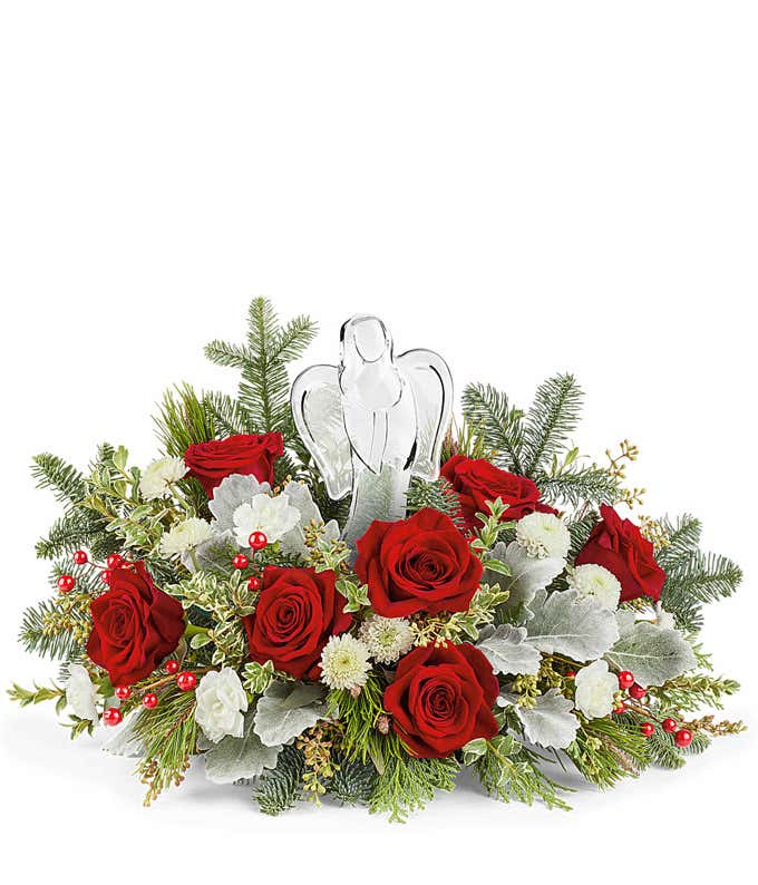 Christmas floral centerpiece with red roses, white chrysanthemums, frosted greenery, red berry accents, and a clear glass angel figurine in the center.