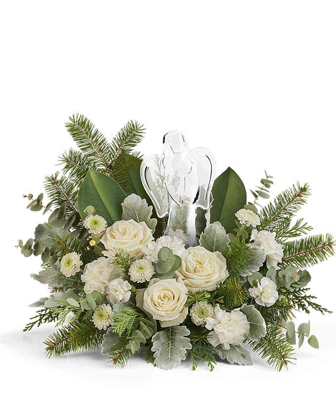 Christmas floral centerpiece with white roses, miniature white carnations, white button spray chrysanthemums, frosted greenery, and a clear glass angel figurine in the center.