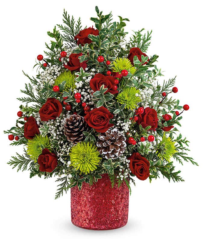Christmas tree-shaped floral arrangement with red roses, green button spray chrysanthemums, white limonium, red berry spray, pinecones, and greenery in a red glittered container.