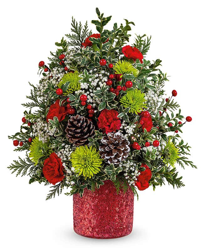 Christmas tree-shaped floral arrangement with red roses, green button spray chrysanthemums, white limonium, red berry spray, pinecones, and greenery in a red glittered container.