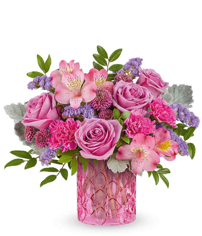 Lavender Roses, Pink Alstroemeria, Fuchsia Carnations, Purple Button Poms, and Floral Greenery in a Pink Glass Short Cylinder Vase