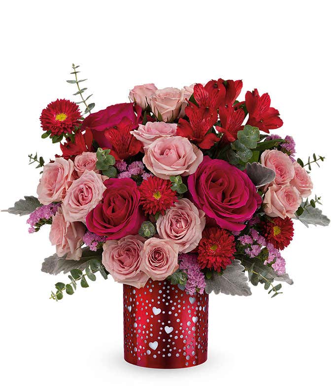 Red and blush rose arrangement with red alstroemeria, pink spray roses, red poms, and eucalyptus, styled in a red keepsake vase with heart cutout accents