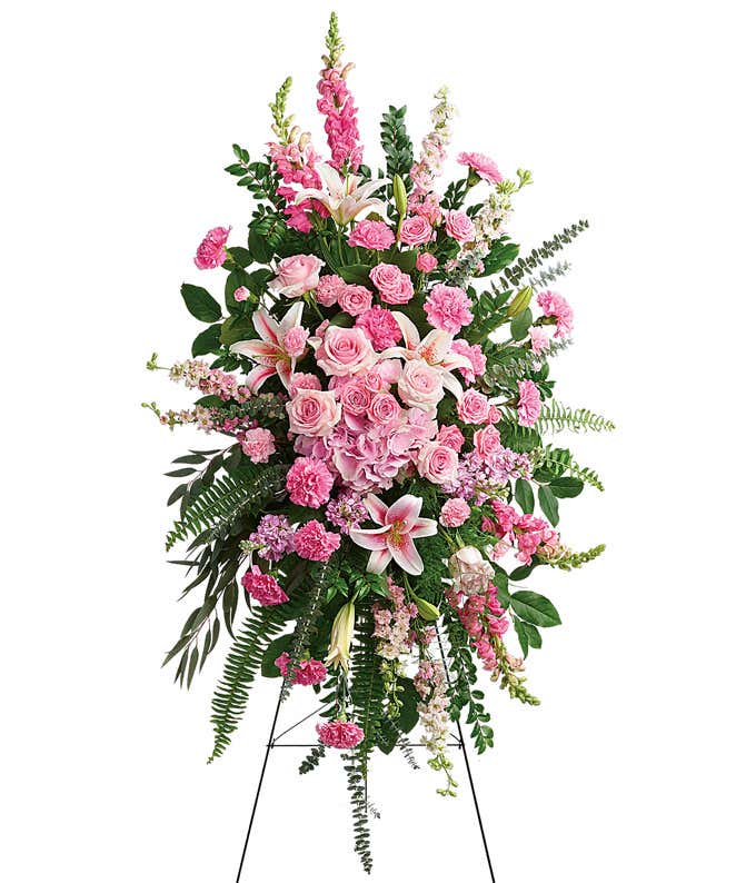 Standing spray with pink roses, lilies, carnations, and green ferns on a metal easel.