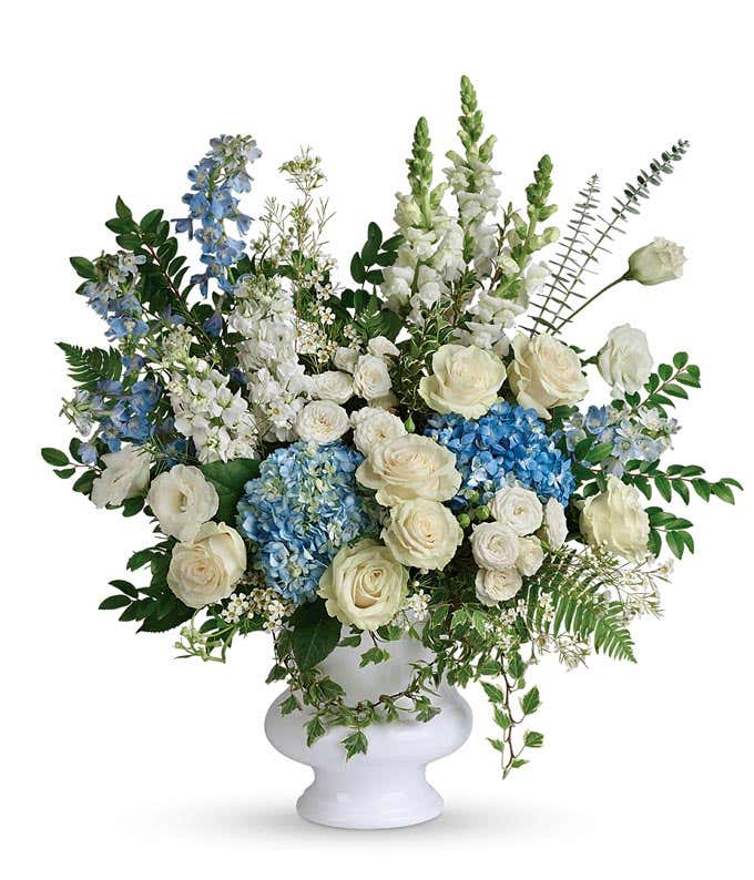 Funeral Bouquet: Light blue hydrangea, white roses, spray roses, lisianthus, delphinium, snapdragons, stock flowers, and floral greenery in a white ceramic vase, symbolizing tranquility and remembrance.