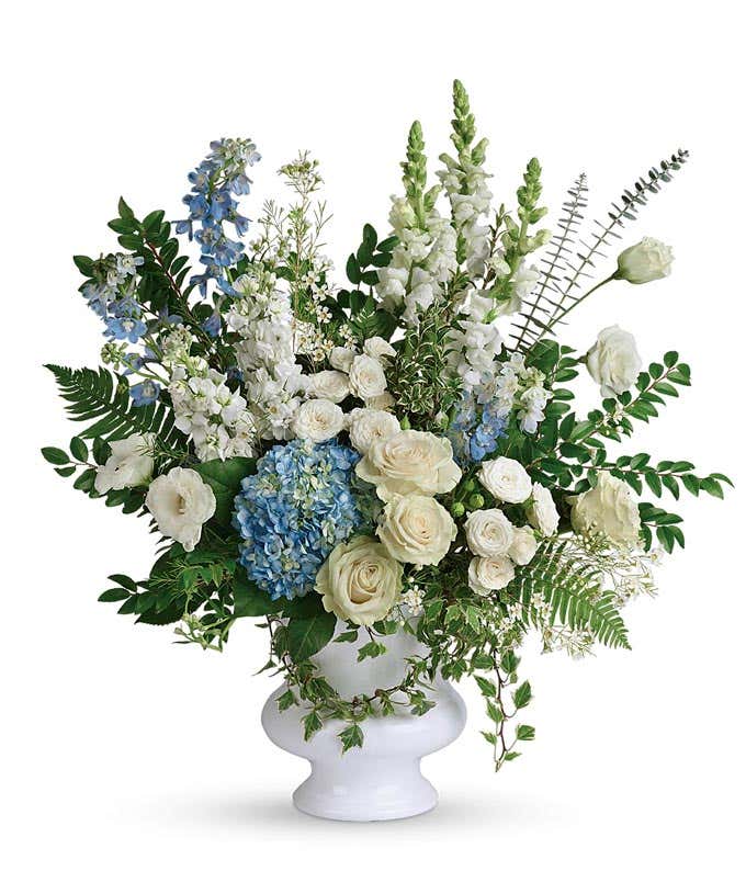 Funeral Bouquet: Light blue hydrangea, white roses, spray roses, lisianthus, delphinium, snapdragons, stock flowers, and floral greenery in a white ceramic vase, symbolizing tranquility and remembrance.