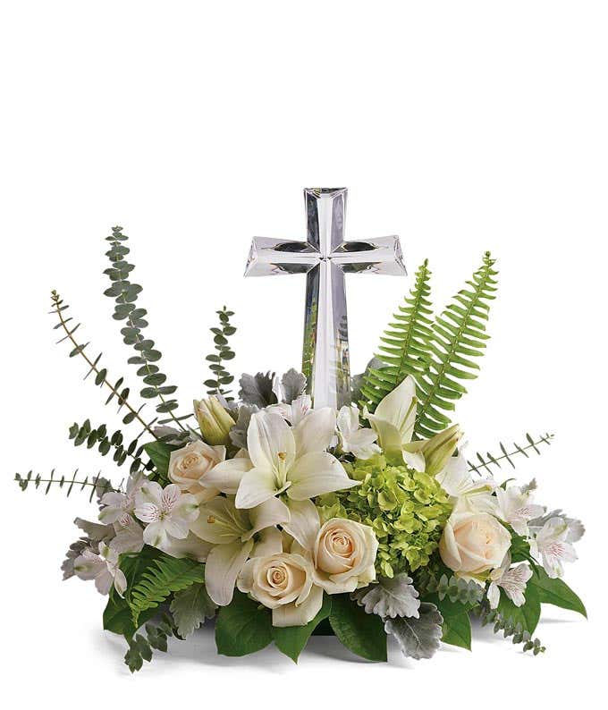 An arrangement of white asiatic lilies, creme roses, and white alstromeria with floral greens and a crystal cross