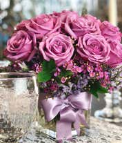 Alternative image 3 for A striking arrangement featuring purple roses, seasonal greens, elegantly presented in a square glass vase adorned with a purple ribbon. This beautiful combination offers a luxurious and sophisticated display, perfect for any special occasion.