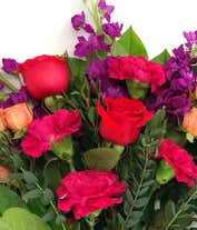 Alternative image 1 for Floral arrangement featuring orange roses, orange spray roses, fuchsia stock, pink carnations, spiral eucalyptus, and lemon leaf with a 'Happy Birthday' pick in a clear cube vase.