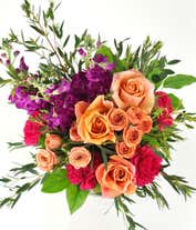 Alternative image 2 for Floral arrangement featuring orange roses, orange spray roses, fuchsia stock, pink carnations, spiral eucalyptus, and lemon leaf with a 'Happy Birthday' pick in a clear cube vase.
