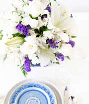 Alternative image 4 for Floral arrangement featuring crème roses, crème spray roses, white Asiatic lilies, white miniature carnations, and purple statice in a blue cube vase.