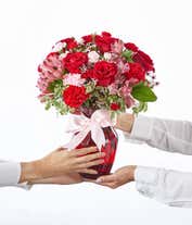 Alternative image 4 for A striking arrangement featuring red roses, pink alstroemeria, red carnations, and pink waxflower, elegantly presented in a red vase with a ribbon. This bold mix offers a stunning and romantic display.