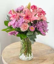 Alternative image 2 for Floral arrangement featuring pink roses, pink Asiatic lilies, pink carnations, pink Matsumoto asters, lavender cushion spray chrysanthemums, pink statice, dusty miller, lemon leaf, in a clear vase.