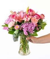 Alternative image 3 for Floral arrangement featuring pink roses, pink Asiatic lilies, pink carnations, pink Matsumoto asters, lavender cushion spray chrysanthemums, pink statice, dusty miller, lemon leaf, in a clear vase.