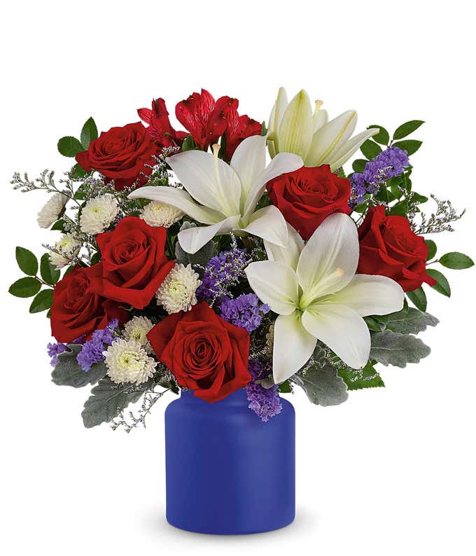 Patriotic arrangement with Red Roses, White Asiatic Lilies, Red Alstroemeria, White Button Spray Chrysanthemums, and a Matte Cobalt Blue Vase.