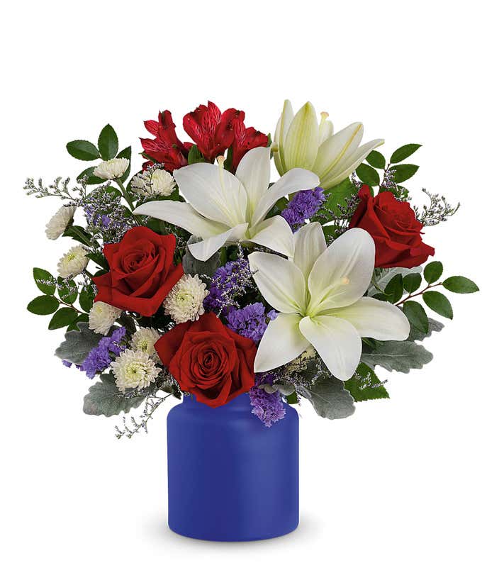 Patriotic arrangement with Red Roses, White Asiatic Lilies, Red Alstroemeria, White Button Spray Chrysanthemums, and a Matte Cobalt Blue Vase.